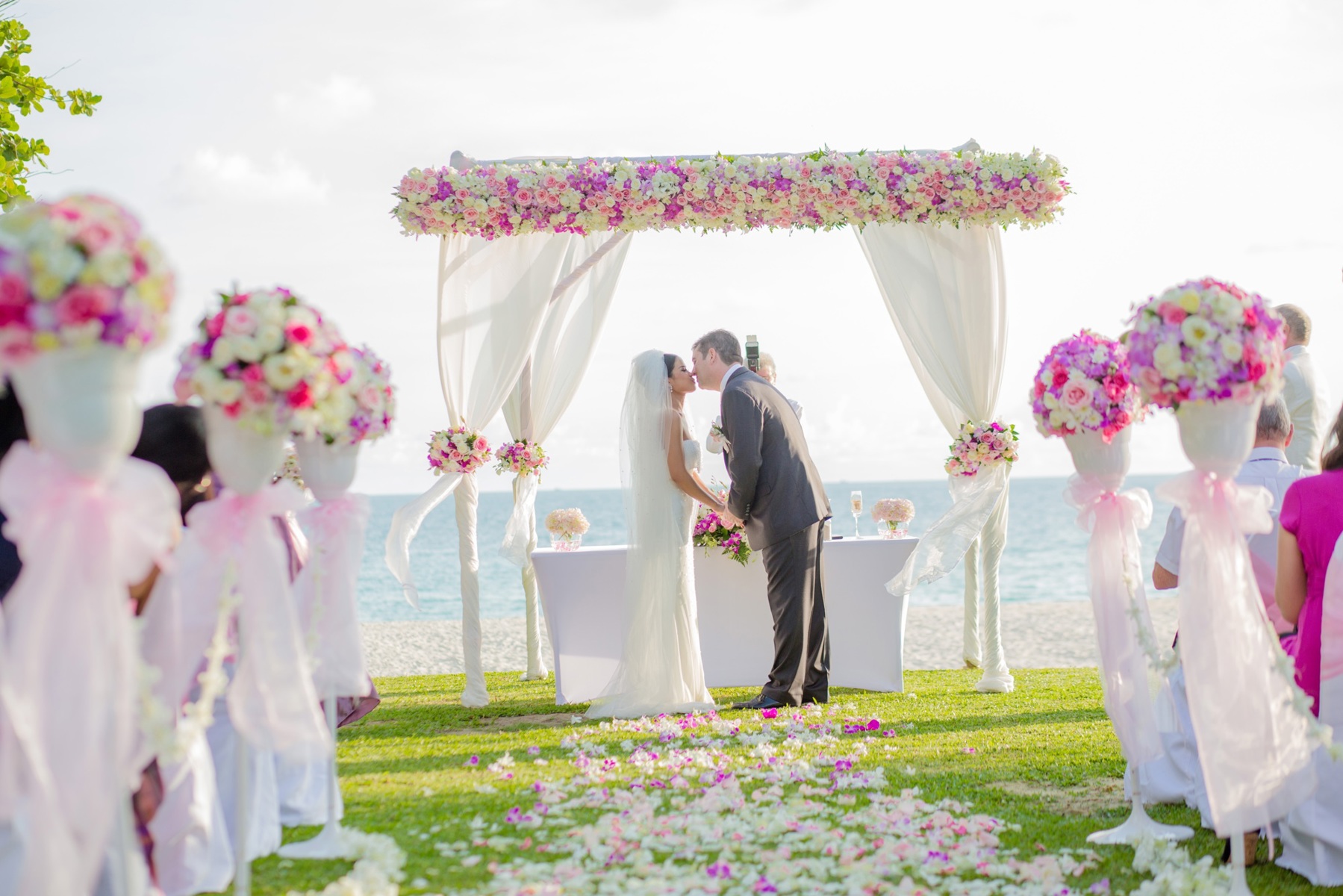 Bride and groom kissing beneath a floral beach wedding canopy, representing destination wedding planning